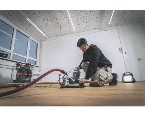 Ein Mann arbeitet mit einer Metabo Kapp- und Gehrungssäge in einem Raum mit Holzboden.