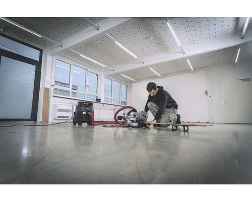 Un homme travaille avec une scie à onglet dans une pièce lumineuse avec un aspirateur