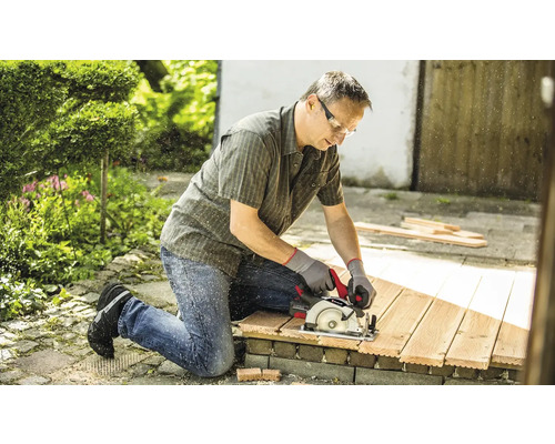 Homme coupant du bois avec une scie circulaire à main dans le jardin.
