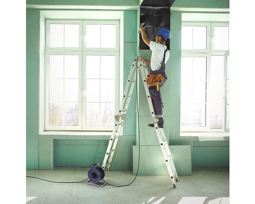 Handwerker auf einer Leiter befestigt Schallschutzplatten an einer Wand in einem Raum.