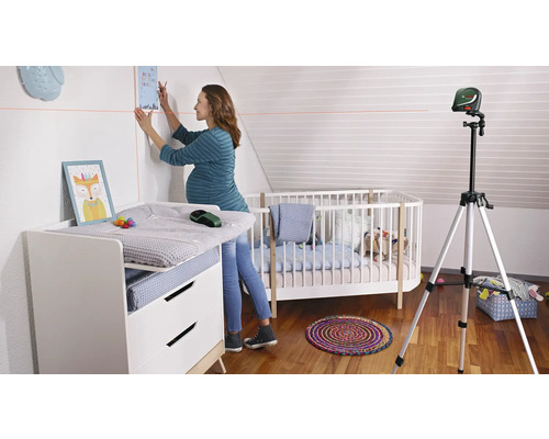 Une femme enceinte utilise un laser linéaire pour accrocher une photo dans une chambre d''enfant. La pièce contient une table à langer et un berceau.
