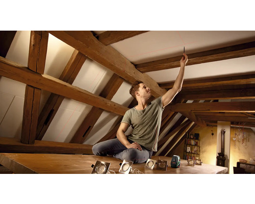 Homme utilisant un niveau laser pour aligner des spots de plafond sous des poutres en bois