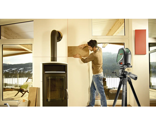 Un homme pose des carreaux avec un laser lignes croisées pour l''alignement à l''intérieur, à côté d''une cheminée.
