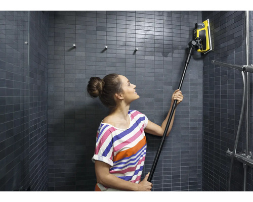 Femme nettoie une douche carrelée avec un racloir à vitre à manche télescopique