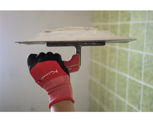 Hand mit Arbeitshandschuh hält eine Glättkelle mit Spachtelmasse