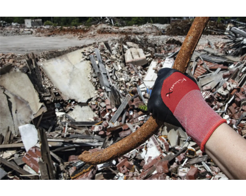 Ein Arbeiter mit Handschuhen hält einen verbogenen Bolzen vor einem Trümmerhaufen.