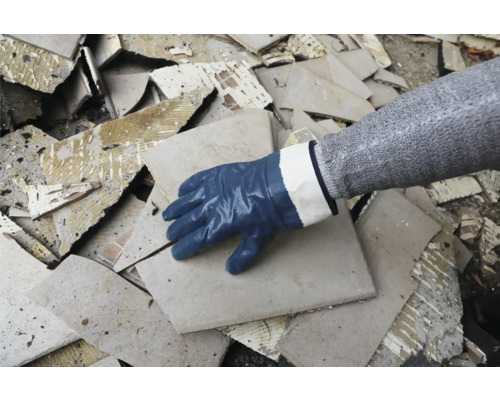 Eine Hand mit Schutzhandschuh auf einem Haufen Fliesenbruch