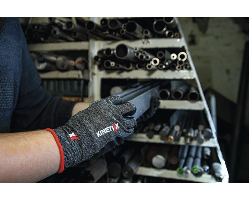 Une personne porte des gants de travail KinetiXx et retire une pièce métallique d''une étagère contenant des tubes métalliques.