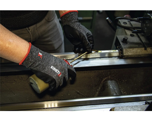 Personne portant des gants de travail KinetiXx travaillant sur une machine.