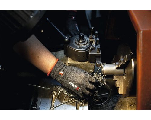 Une personne porte des gants de travail sur un tour avec des copeaux de métal.