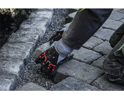 Eine Person verlegt Pflastersteine mit Schutzhandschuhen.