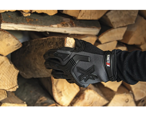 Hand mit Arbeitshandschuh hält Holzscheit vor Holzstapel