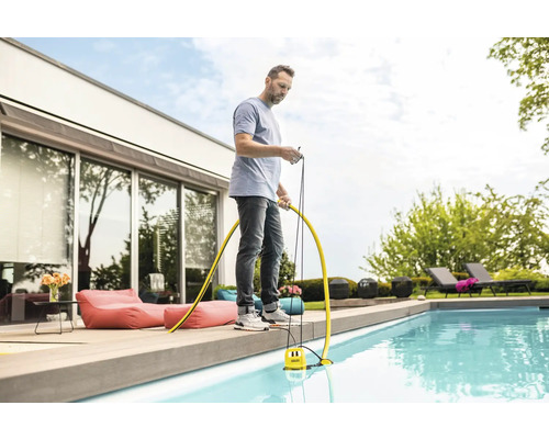 Un homme utilise une pompe de piscine pour nettoyer la piscine dans le jardin