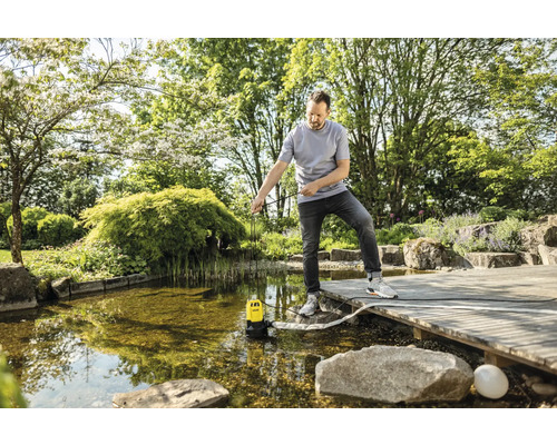 Un homme utilise une pompe submersible dans un bassin de jardin.