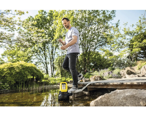 Un homme utilise une pompe à eau sale près d''un étang dans le jardin.