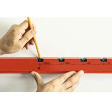 Hand mit Bleistift markiert Dübellöcher an einer Wand mit einer Bohrschablone.