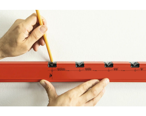 Hand mit Bleistift markiert Dübellöcher an einer Wand mit einer Bohrschablone.