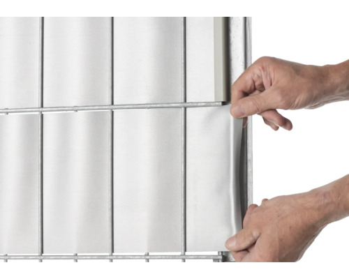 Une personne fixe des bandes de confidentialité sur une clôture à double barre.