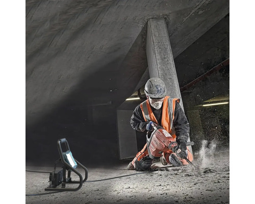 Ouvrier du bâtiment travaillant au marteau-piqueur sous un pont en béton, projecteur de chantier éclairant le chantier