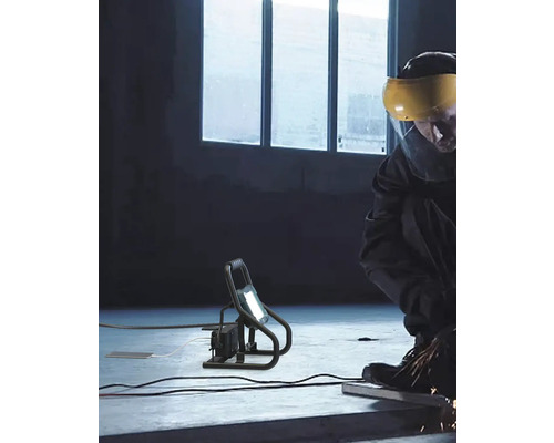 Ouvrier avec visière de protection et projecteur de chantier LED dans un atelier