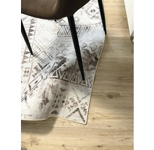 Dekorativer Teppich mit geometrischen Mustern unter einem Stuhl auf Holzboden.