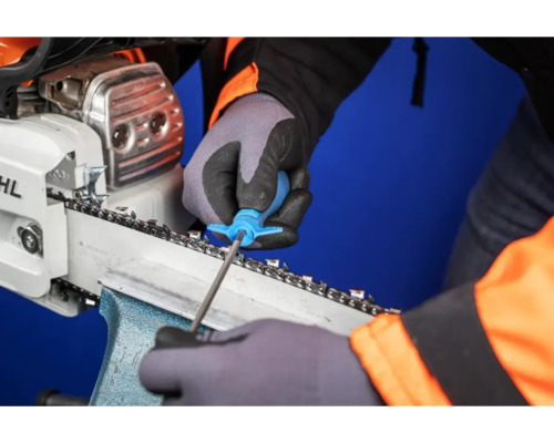 Une personne affûte une tronçonneuse avec un outil.