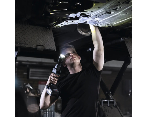 Un homme inspecte le dessous d''une voiture avec une lampe de travail LED.