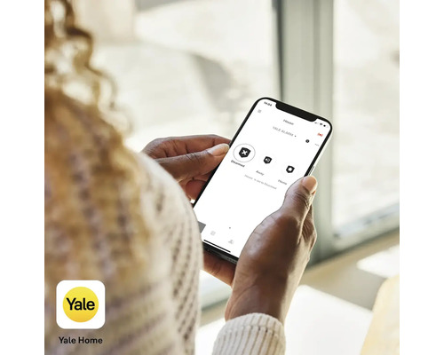 Une personne utilise l''application Yale Home sur un smartphone pour commander un système d''alarme.