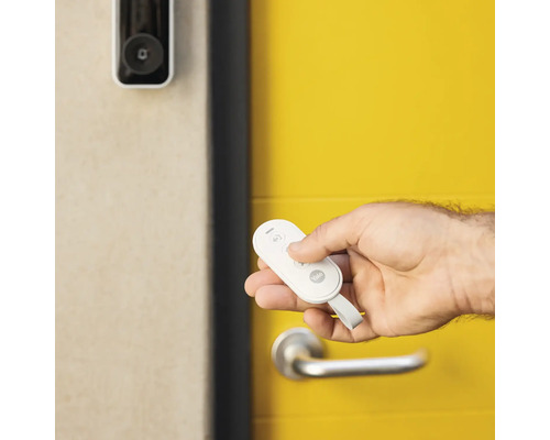 Main avec télécommande Yale devant une porte d''entrée avec caméra vidéo