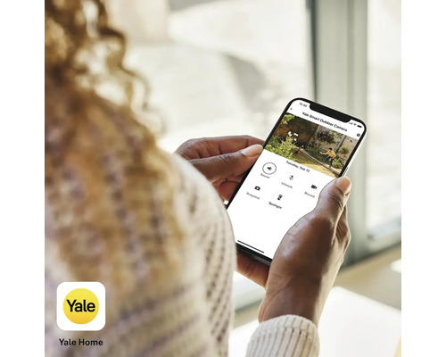 Une personne tient un smartphone avec l''application Yale Smart Outdoor Camera.