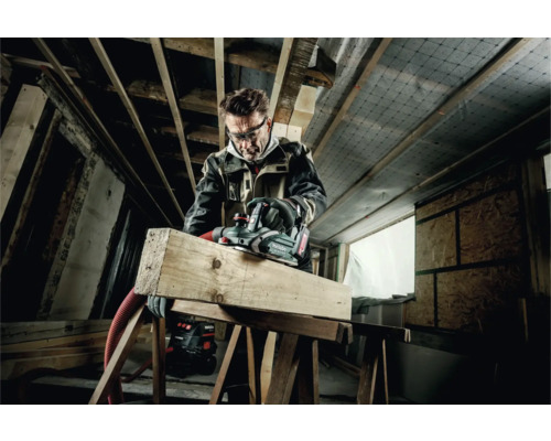 Artisan rabotant des poutres en bois avec un rabot électrique Metabo dans un grenier.