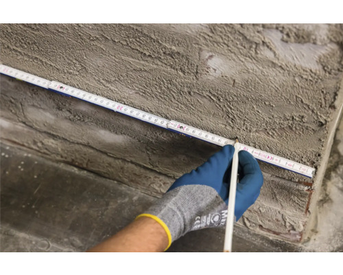 Main avec crayon marquant une mesure sur un mètre pliant sur un mur