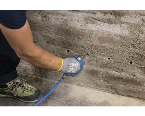 Un homme nettoie les trous de perçage dans un mur avec de l''air comprimé