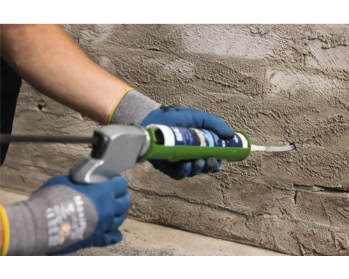 Une personne utilise un pistolet à cartouche sur un mur pour sceller un joint.