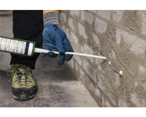 Une personne scelle un mur de briques avec du mastic.