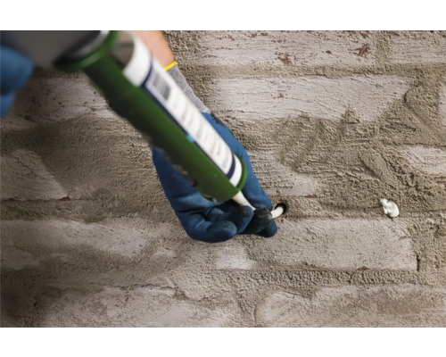 Un artisan remplit un trou dans un mur de pierre avec du mastic