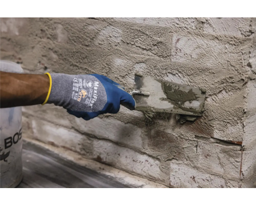 Une personne applique du plâtre sur un mur de briques à l''aide d''une truelle