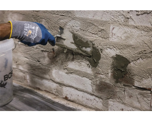 Un artisan joint un mur en briques avec un couteau à mastic et du mortier de jointoiement