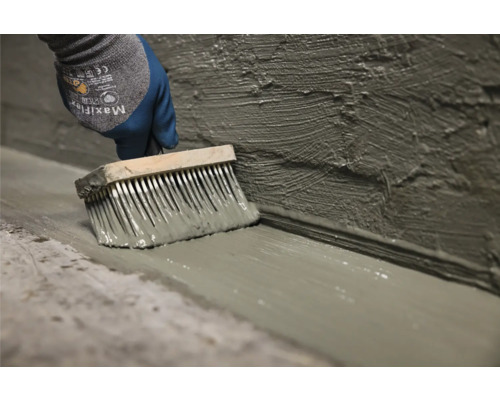 Une personne applique un produit d''étanchéité sur le mur et le sol à l''aide d''un pinceau.