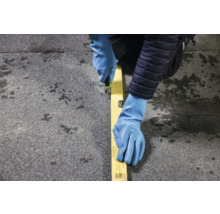 Eine Person mit Handschuhen schneidet mit einem Messer entlang einer Wasserwaage auf einer Oberfläche.