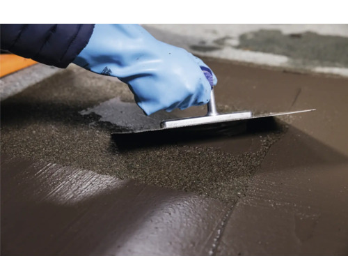 Une personne lisse un enduit de sol avec une spatule.