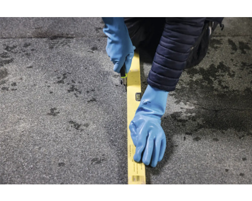 Personne avec des gants de travail, un niveau à bulle et un cutter coupant un matériau