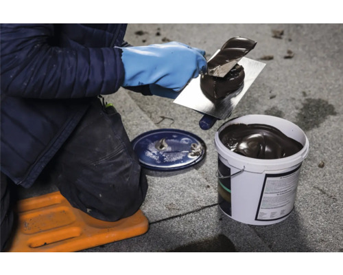 Une personne applique de la colle à toit sur un toit à l''aide d''une truelle, la colle provient d''un seau.