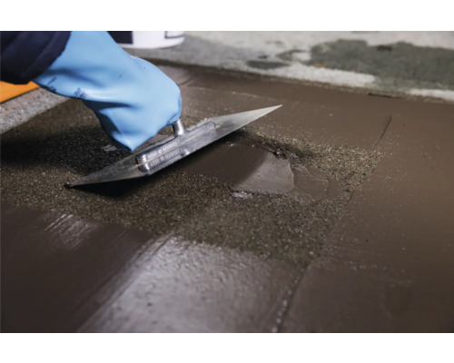 Une personne portant des gants lisse une chape avec une spatule.