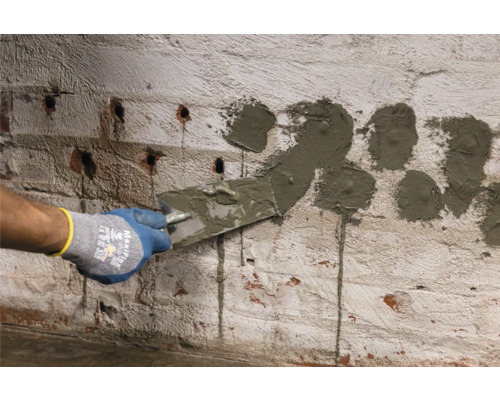 Handwerker füllt Löcher in einer Ziegelmauer mit einer Spachtel.