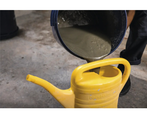 Aus einem Eimer wird Beton in eine gelbe Giesskanne gegossen.