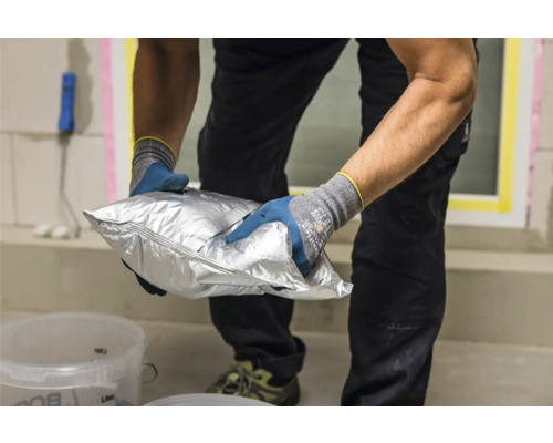 Une personne tient un sac argenté contenant du matériel pour les travaux de construction.