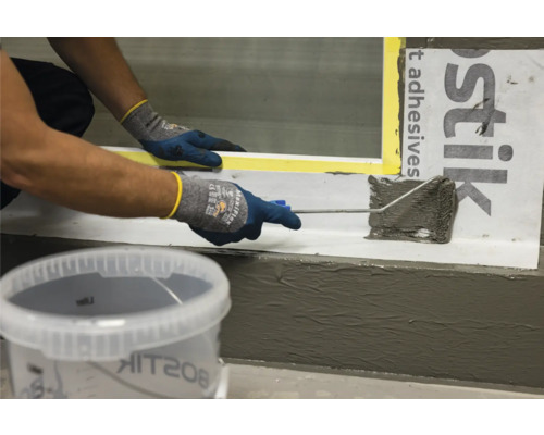 Une personne applique du mastic avec un rouleau, avec le logo Bostik en arrière-plan