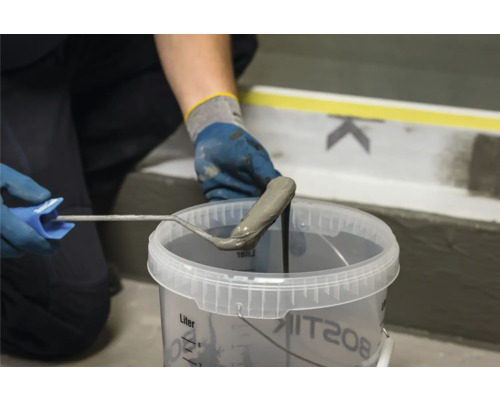 Une personne trempe un rouleau à peinture dans un seau de scellant plastique liquide de Bostik.