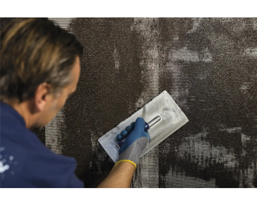 Un homme applique du mortier d''armature sur un tissu à l''aide d''une truelle à plâtre.